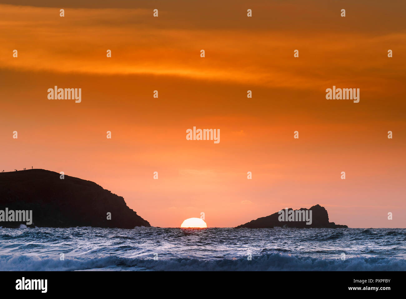 Die Sonne zwischen Ost Pentire Headland und die Gans eine kleine Felseninsel an Fistral in Newquay in Cornwall. Stockfoto