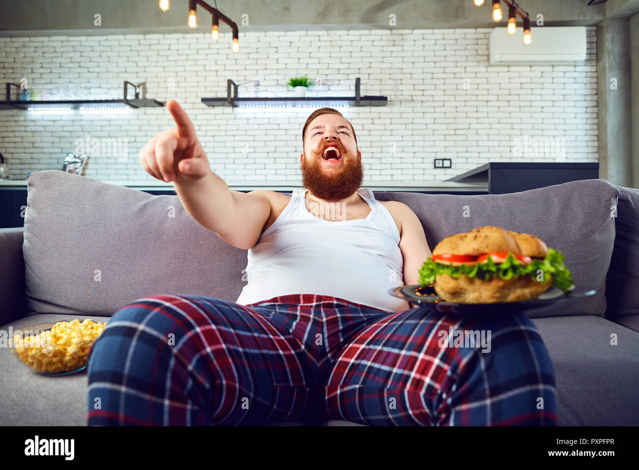 Dicke lustiger Mann mit einem Burger sitzen auf der Couch. Stockfoto