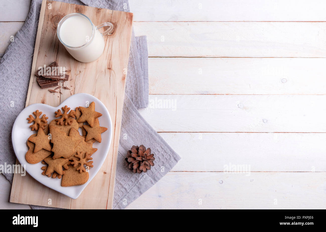 Weihnachten Frühstückstisch mit Lebkuchen Cookies auf eine herzförmige Platte, Schokolade und Milch, auf einer hölzernen Platte, auf einem weißen Holztisch. Stockfoto