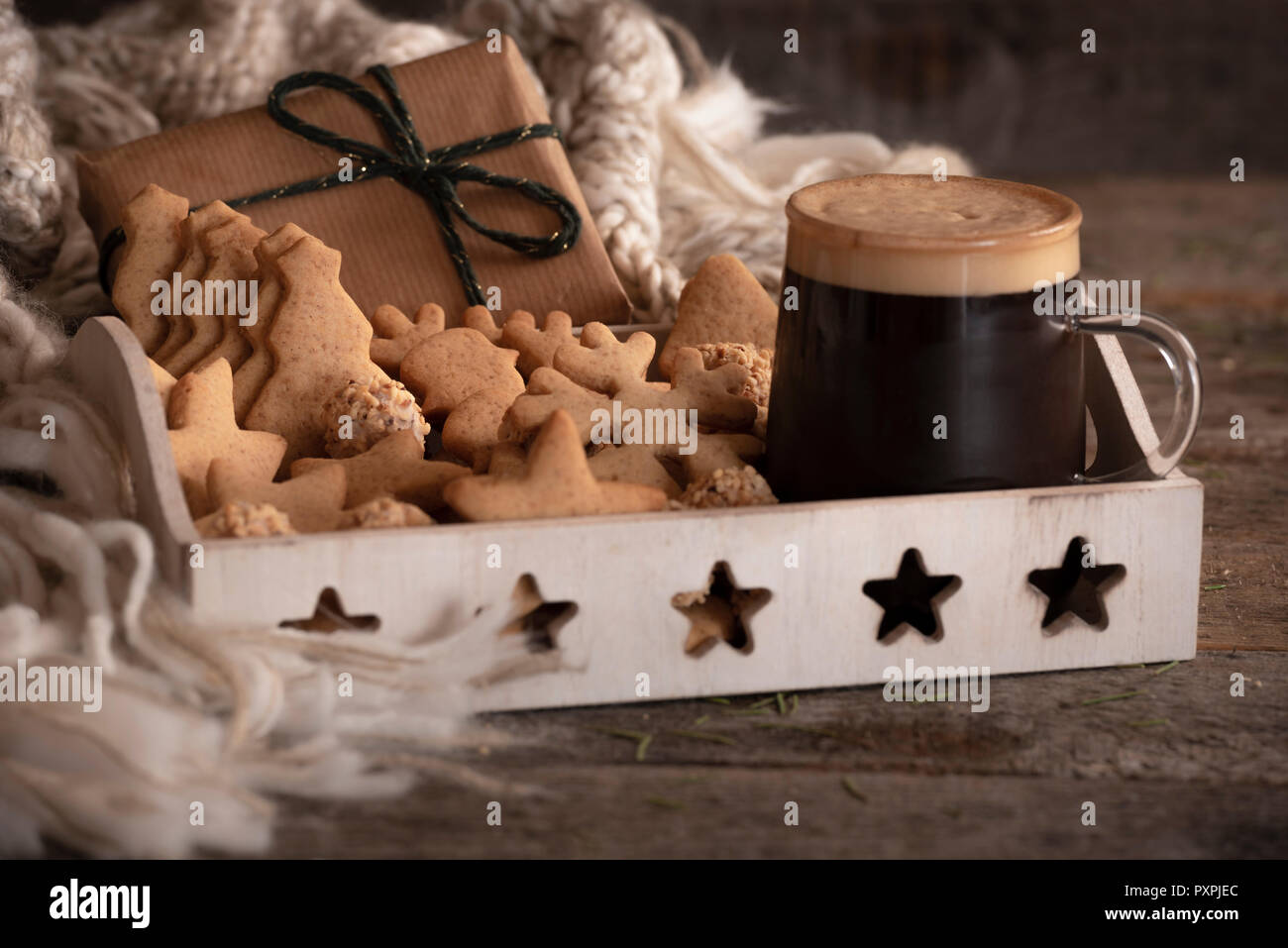 Frühstück Tablett mit einer Tasse Kaffee, Lebkuchen Cookies, und Haselnüsse Bonbons, ein Weihnachtsgeschenk und einen Wollschal, auf einem rustikalen Holztisch. Stockfoto
