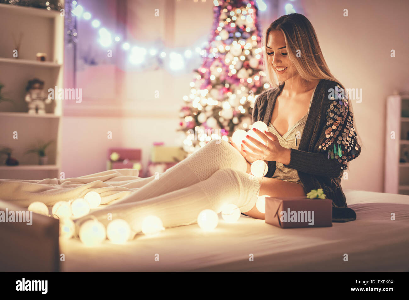 Süße junge lächelnde Frau mit Geschenk und Sitzen im Bett mit Weihnachten bubble Lights. Stockfoto