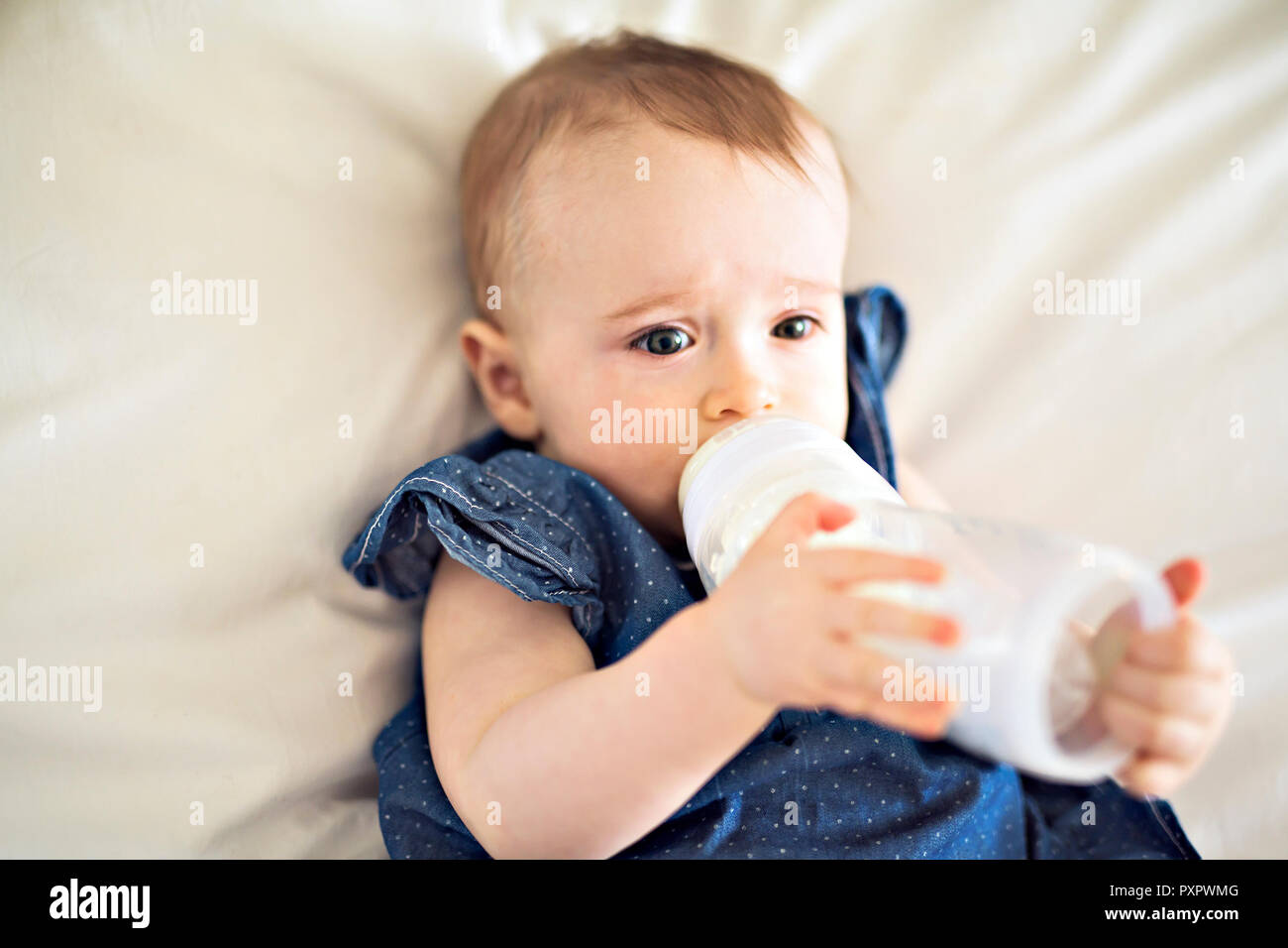 Pretty baby Mädchen trinkt Wasser aus der Flasche liegend auf Bett Stockfoto