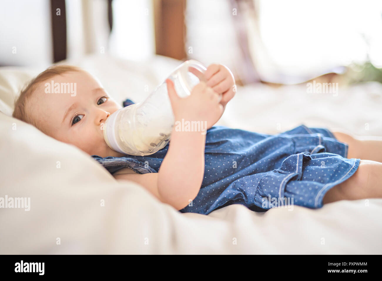 Pretty baby Mädchen trinkt Wasser aus der Flasche liegend auf Bett Stockfoto