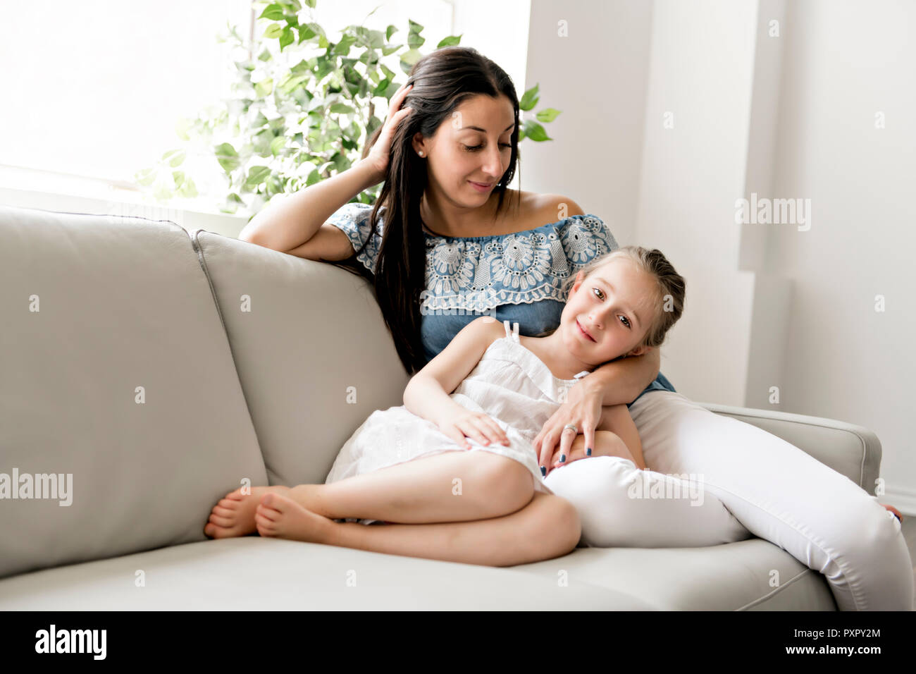 Porträt der schönen Mutter und ihre kleine Tochter sitzen zusammen auf der Couch Stockfoto