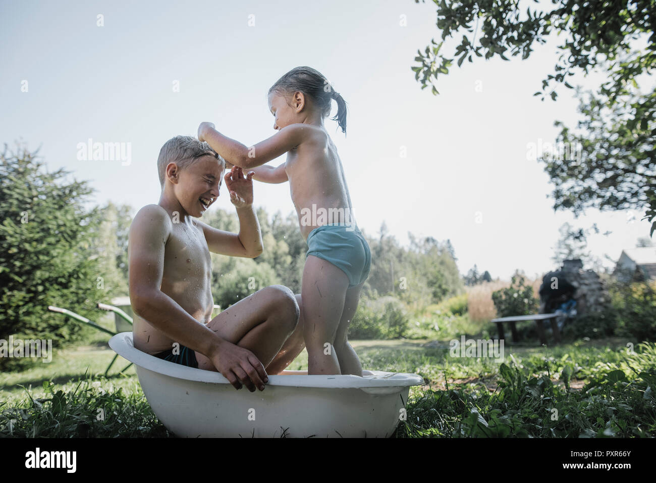 Bruder und Schwester spielen mit Wasser in kleinen Badewanne im Garten Stockfoto