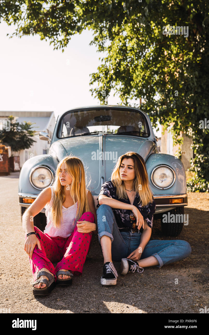 Zwei junge Frauen draußen sitzen bei einem Oldtimer Stockfoto