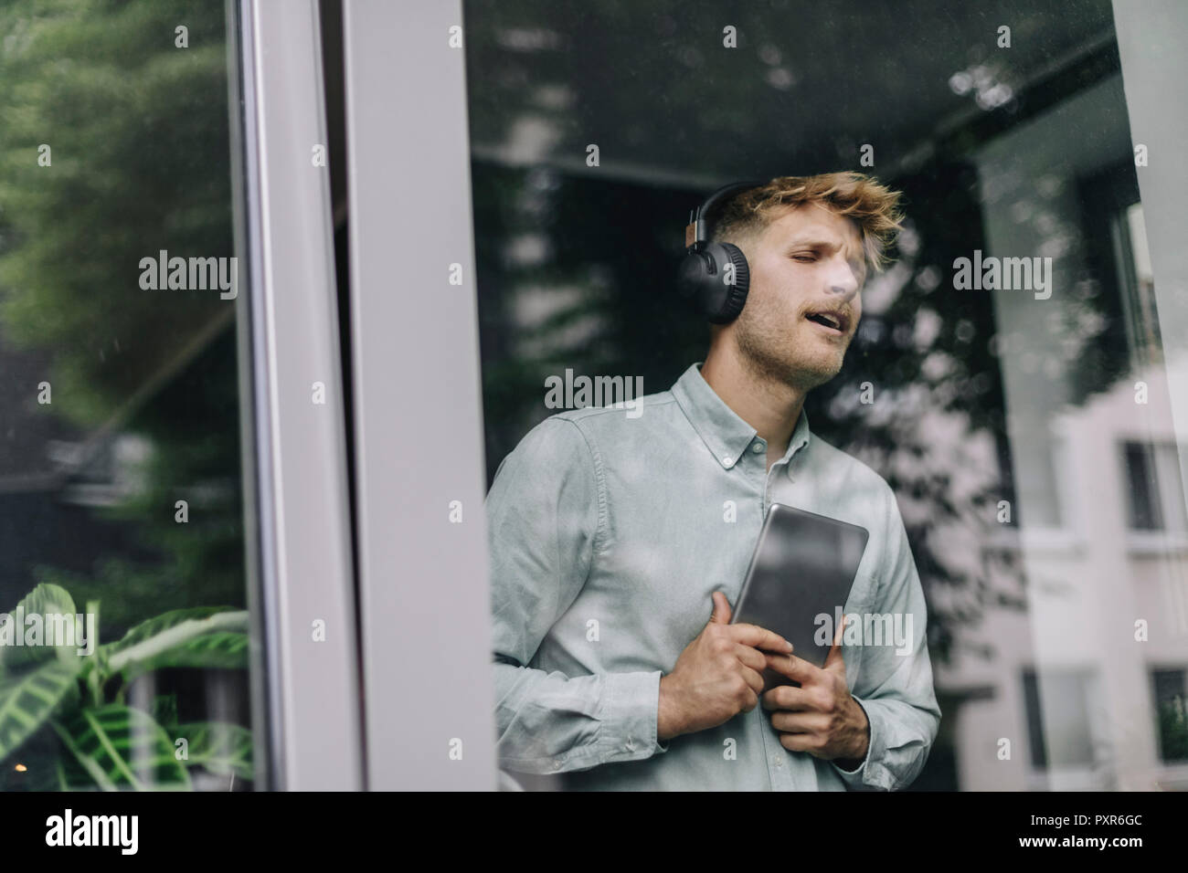 Junge Mann am Fenster, Musik hören mit Kopfhörern und digitale Tablet Stockfoto