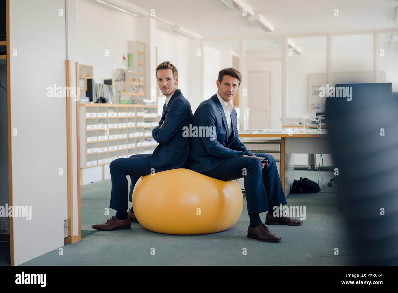 Zwei Unternehmer prüfen Smartphone mit gelben Fitness Ball im Vordergrund. Stockfoto