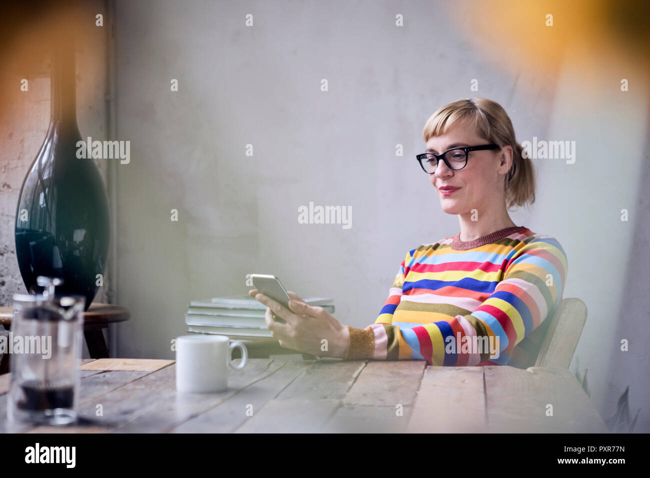 Porträt der lächelnde Frau am Tisch sitzend bei einer Tasse Kaffee in der Zelle Telefon Stockfoto