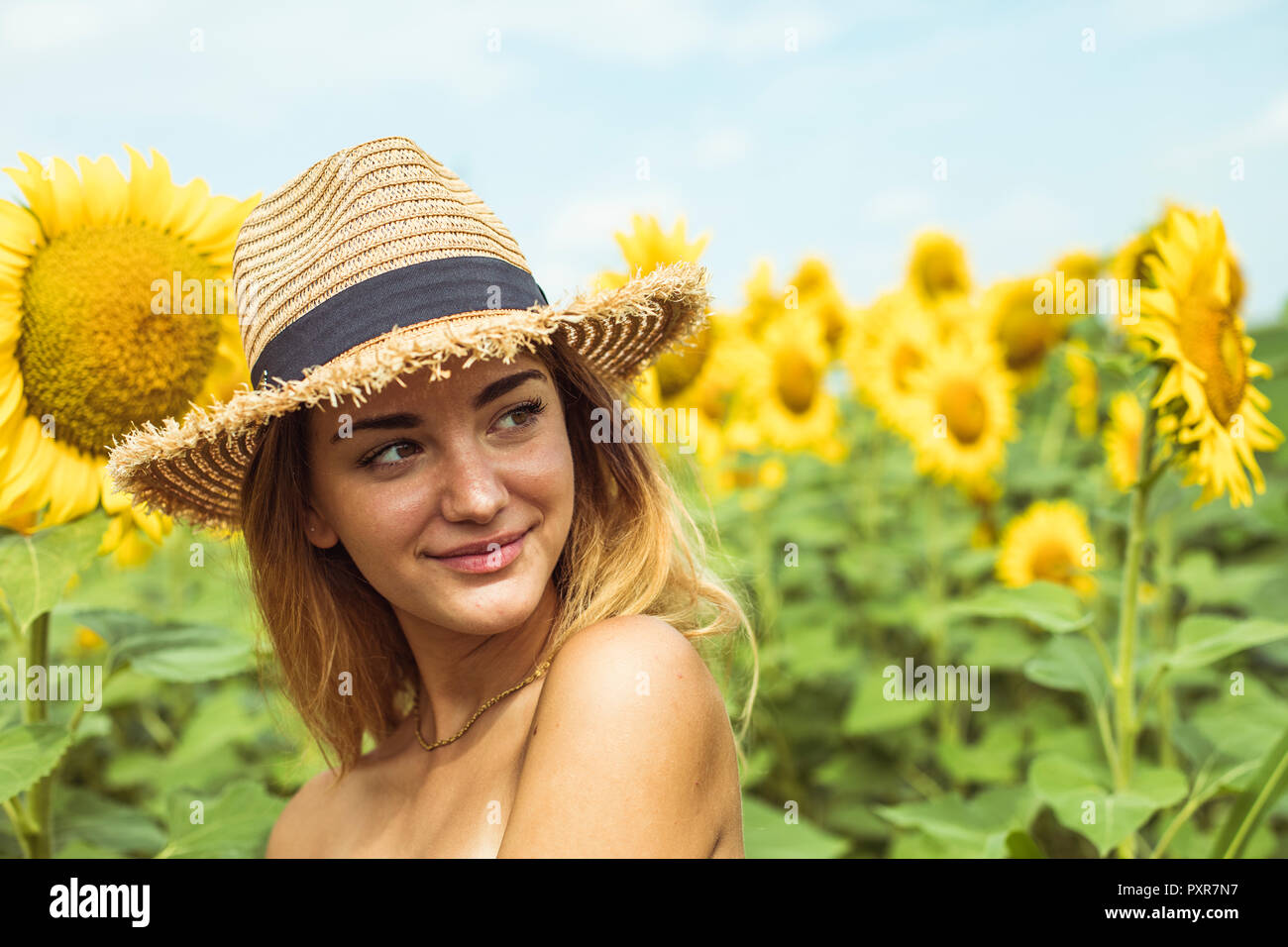 Junge Frau mit einem Strohhut lächelnd in einem Feld mit Sonnenblumen Stockfoto