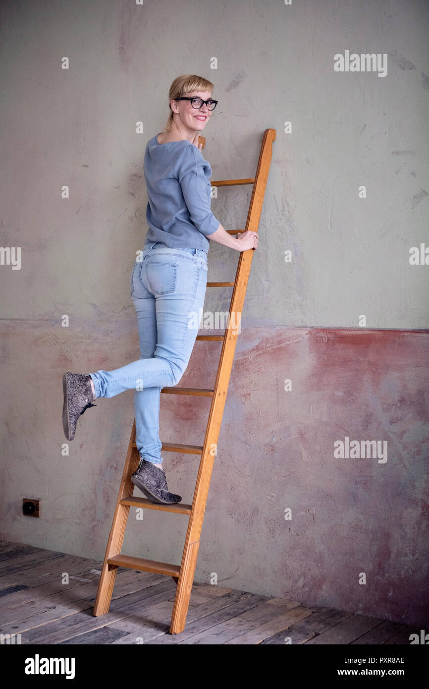 Lächelnde Frau stehend auf die Leiter in einem unrenovierten Zimmer eines Loft Stockfoto