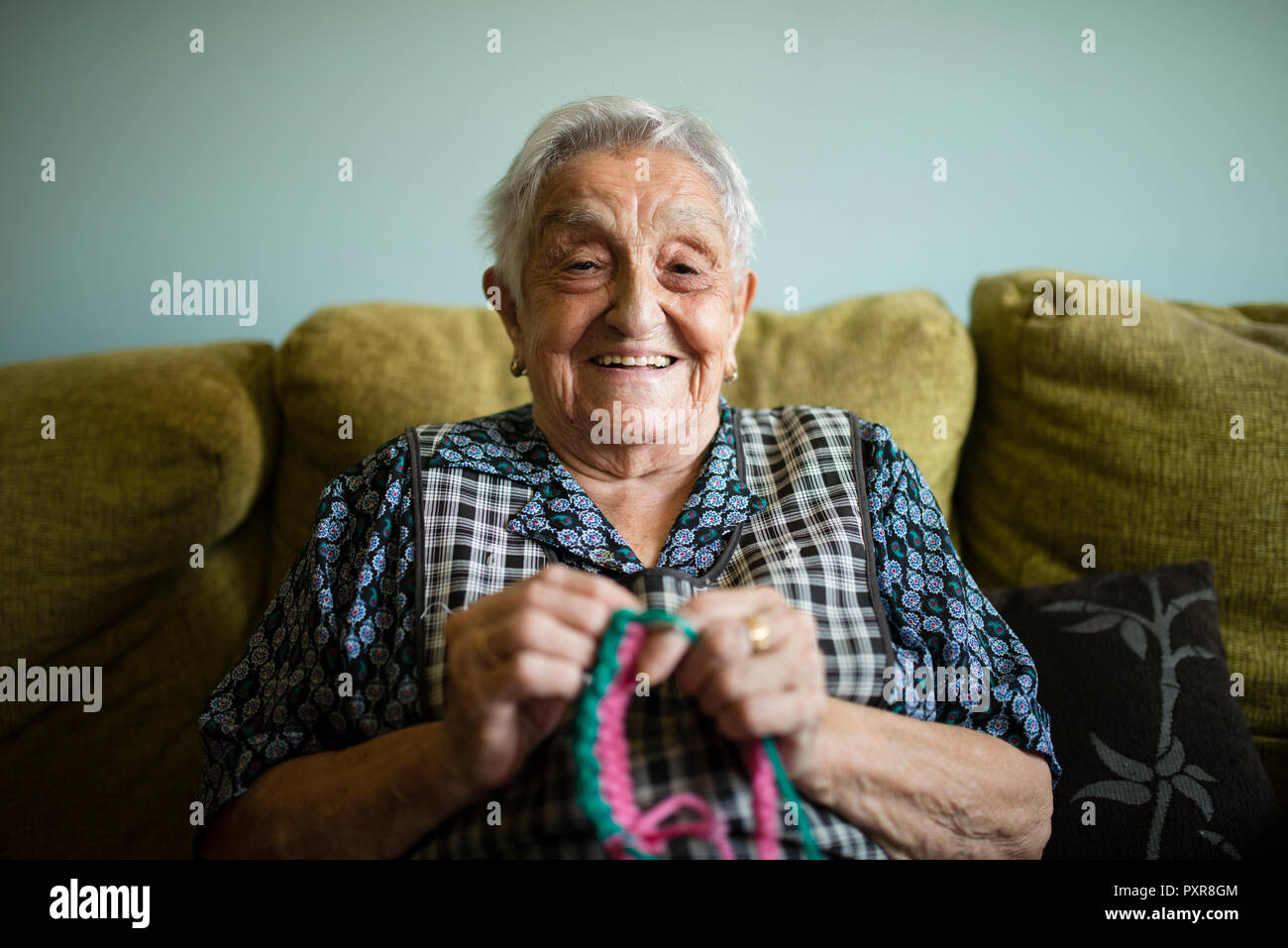 Portrait von lächelnden älteren Frau auf der Couch zu Hause häkeln Stockfoto