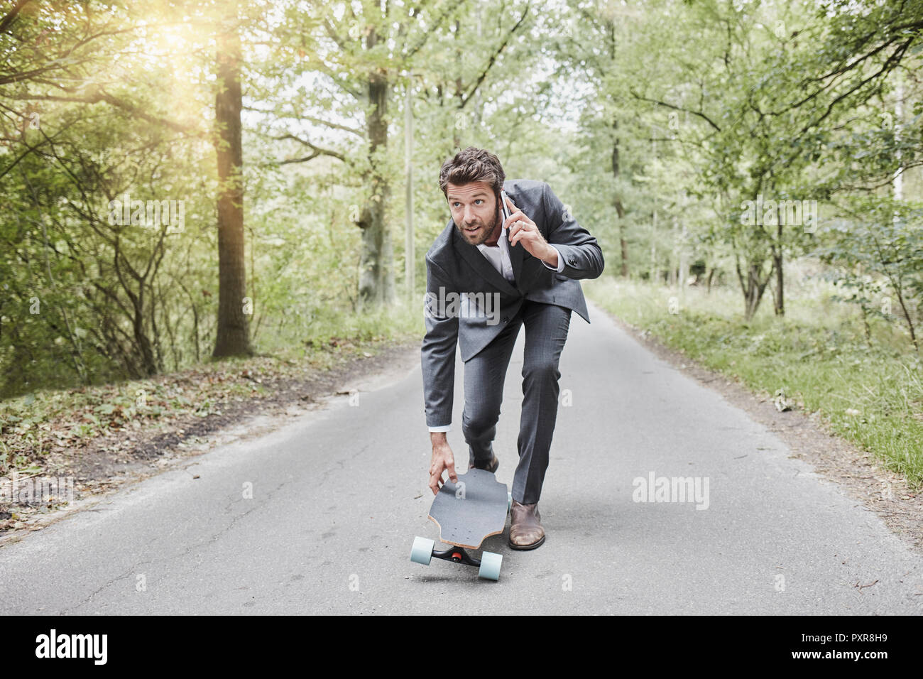 Unternehmer gehen mit Skateboard und Smartphone auf die ländliche Straße Stockfoto