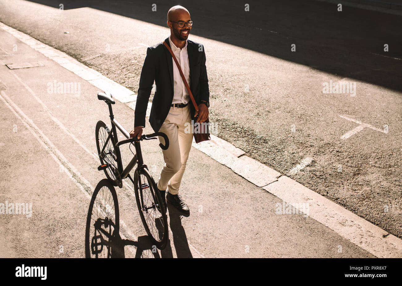 Hübscher junger erwachsener Mann mit Anzug zu Fuß mit seinem Fahrrad im Freien. Afrikanischen Geschäftsmann, Büro mit seinem Fahrrad. Stockfoto