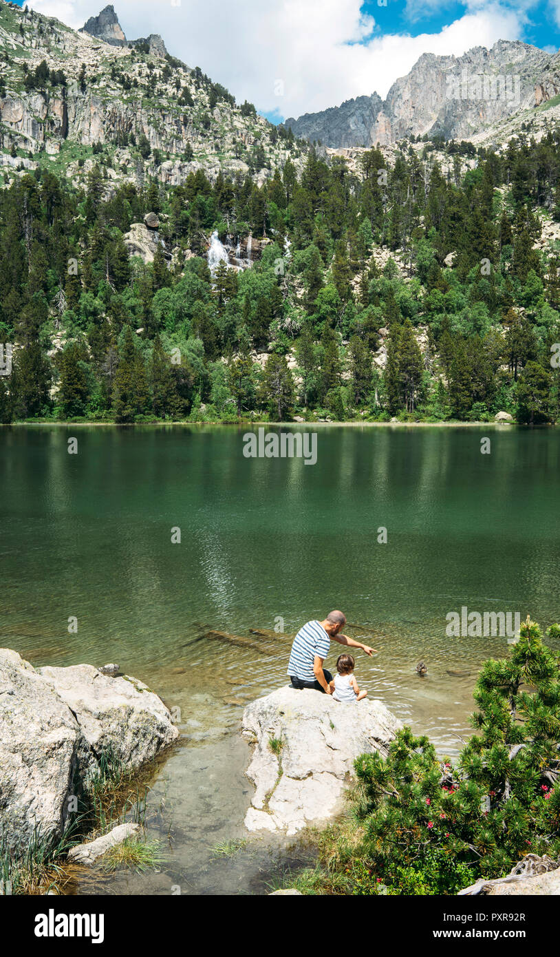 Spanien, Vater und Tochter auf einem Stein saß an einem Bergsee, feeding ducks Stockfoto