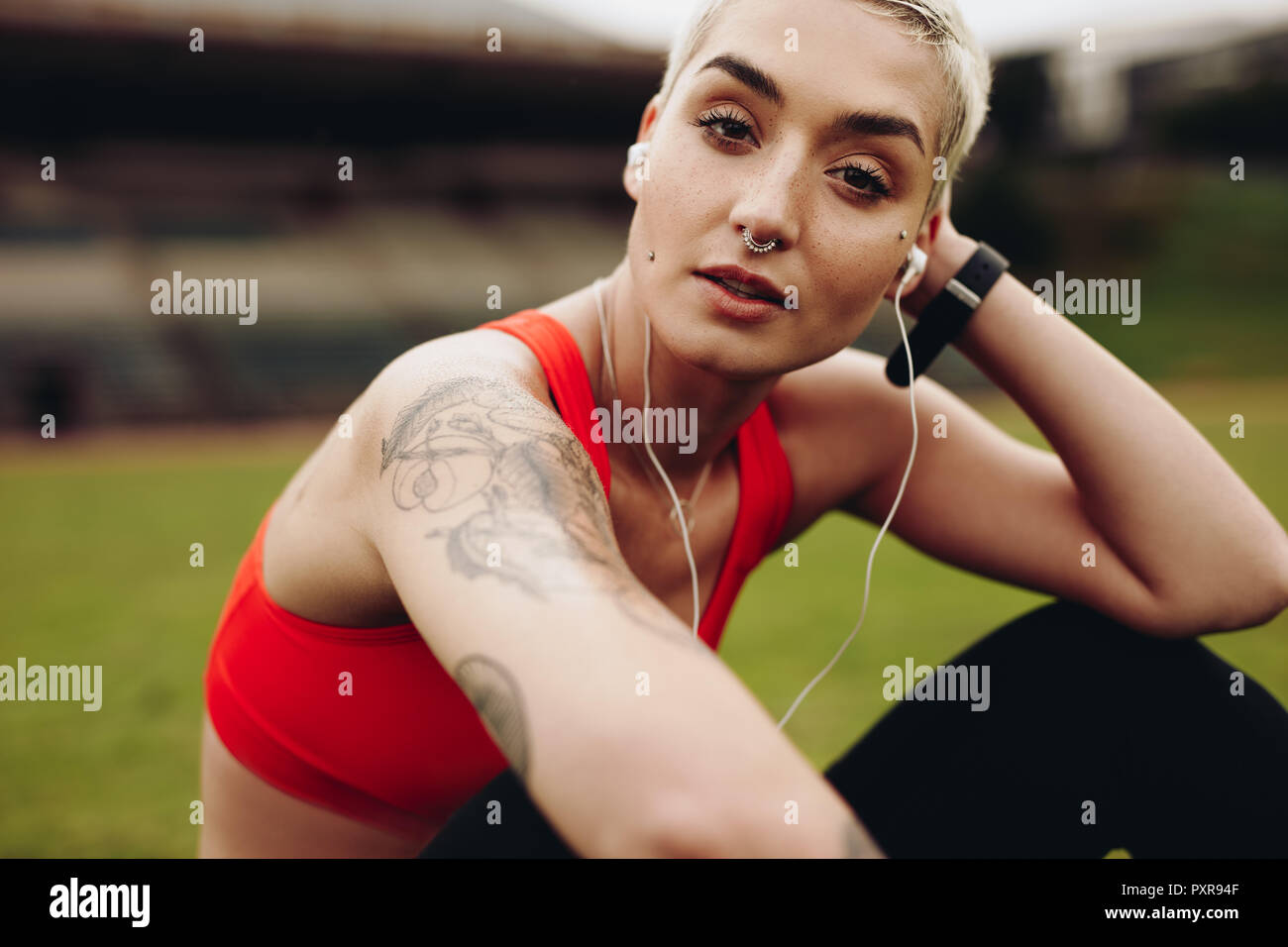 Weibliche Athleten entspannen auf dem Boden sitzend Musik zu hören. Frau in Fitness Kleidung Musikhören mit Kopfhörern sitzen und entspannen in Stockfoto