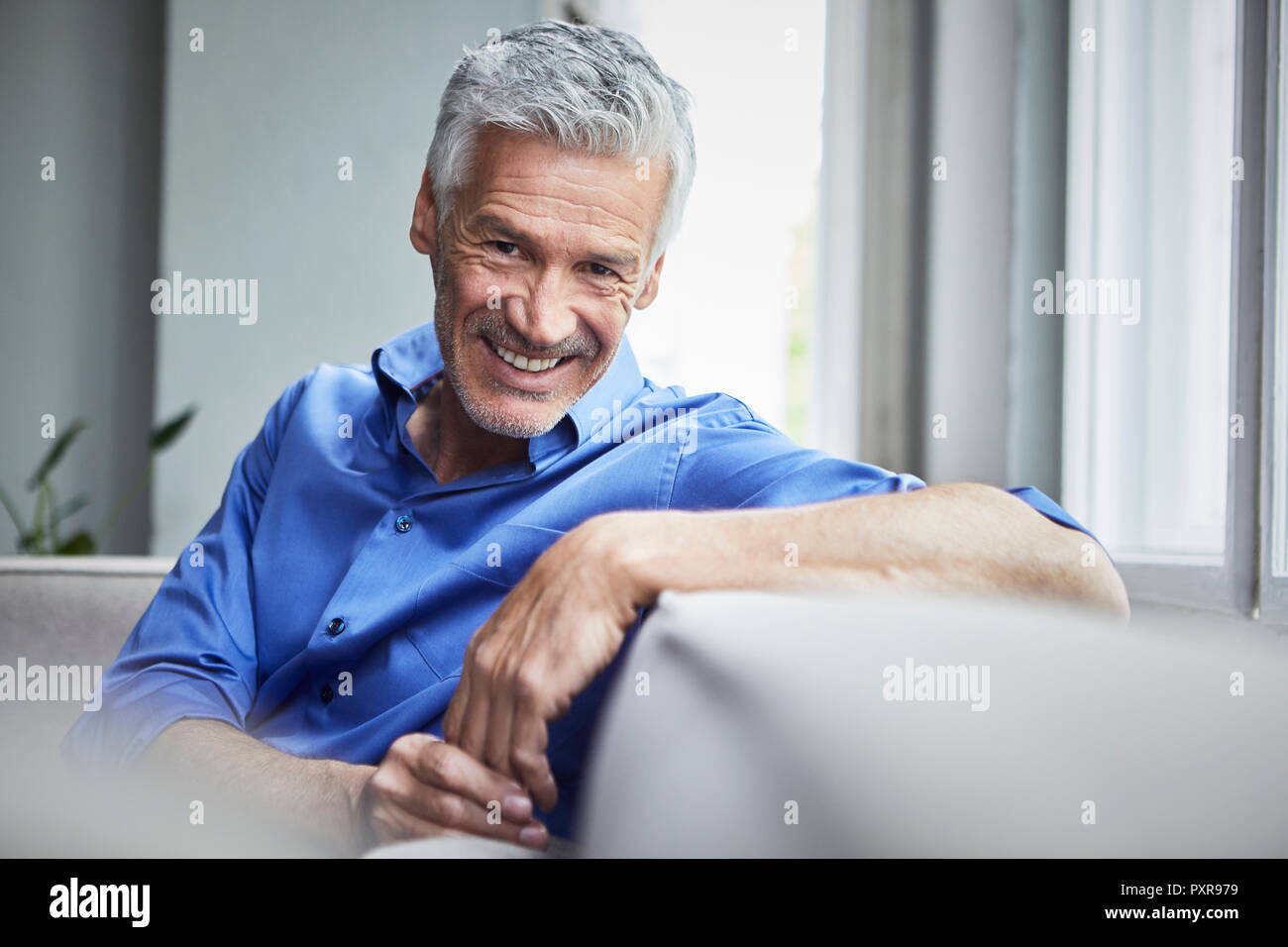 Portrait von lächelnden reifer Mann auf der Couch zu Hause sitzen Stockfoto