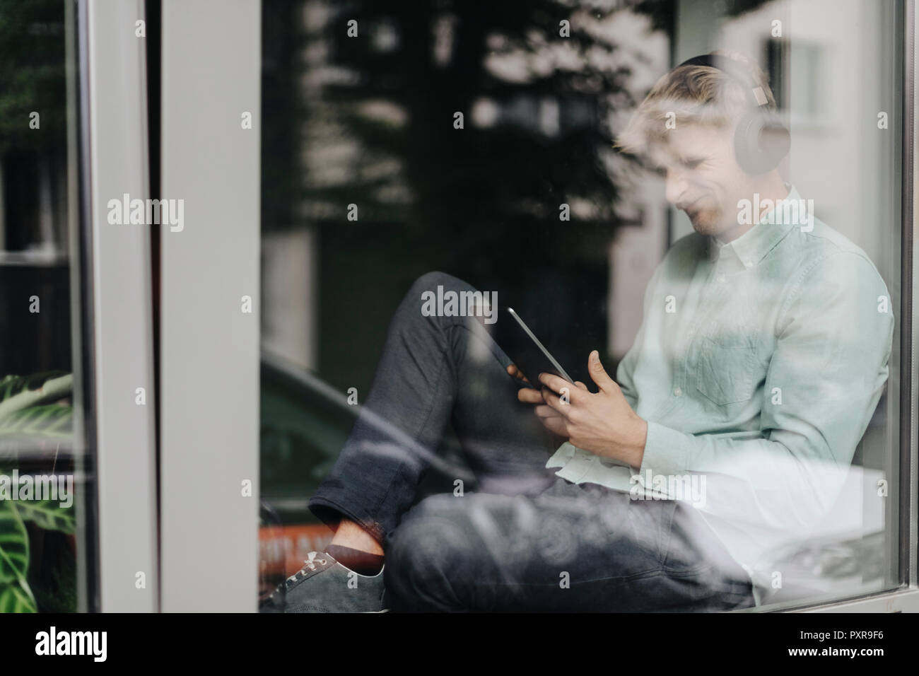Junger Mann am Fenster sitzen, Musik hören mit Kopfhörern und digitale Tablet Stockfoto