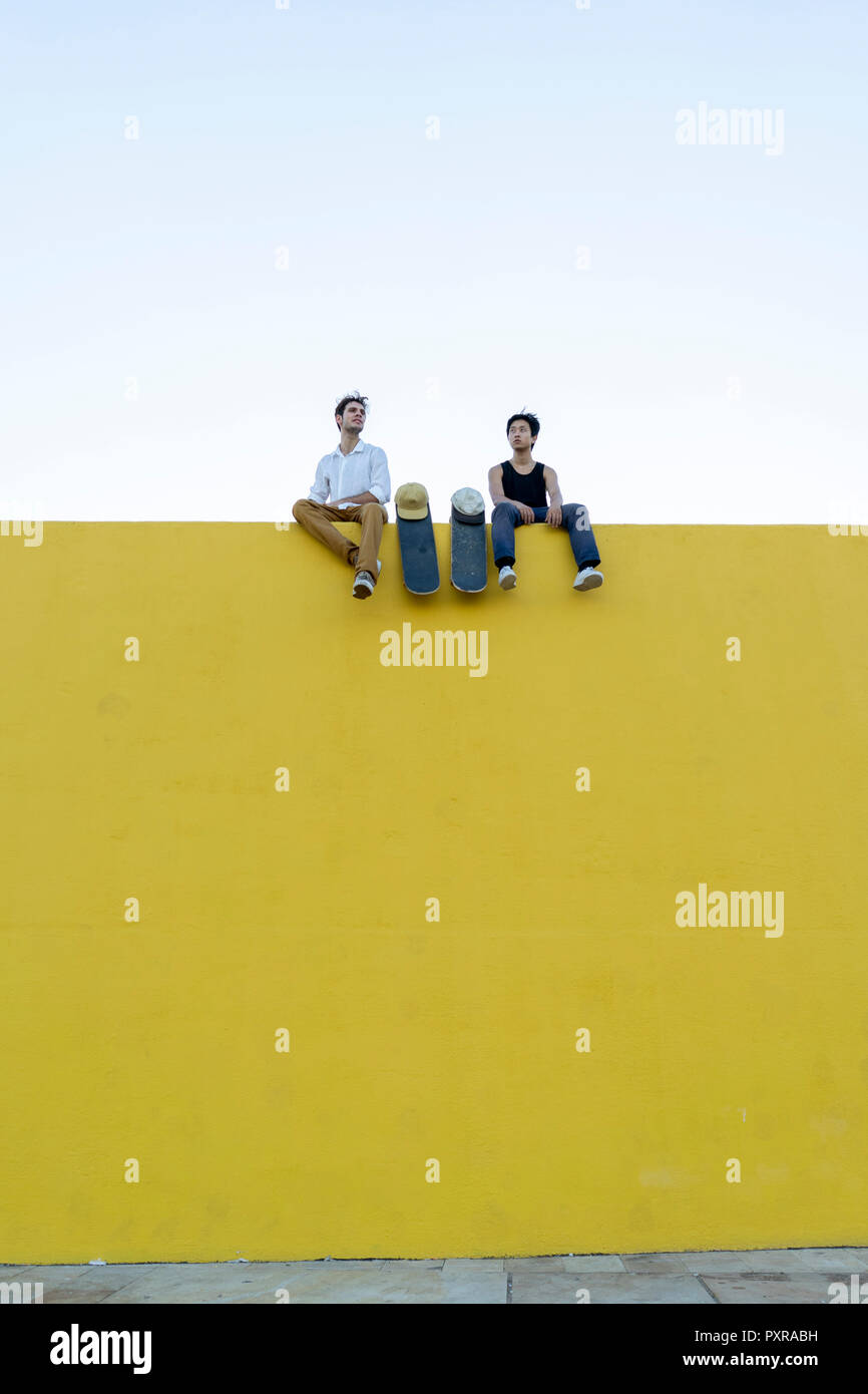 Zwei junge Männer mit skateboards sitzt auf einem hohen gelbe Wand Stockfoto