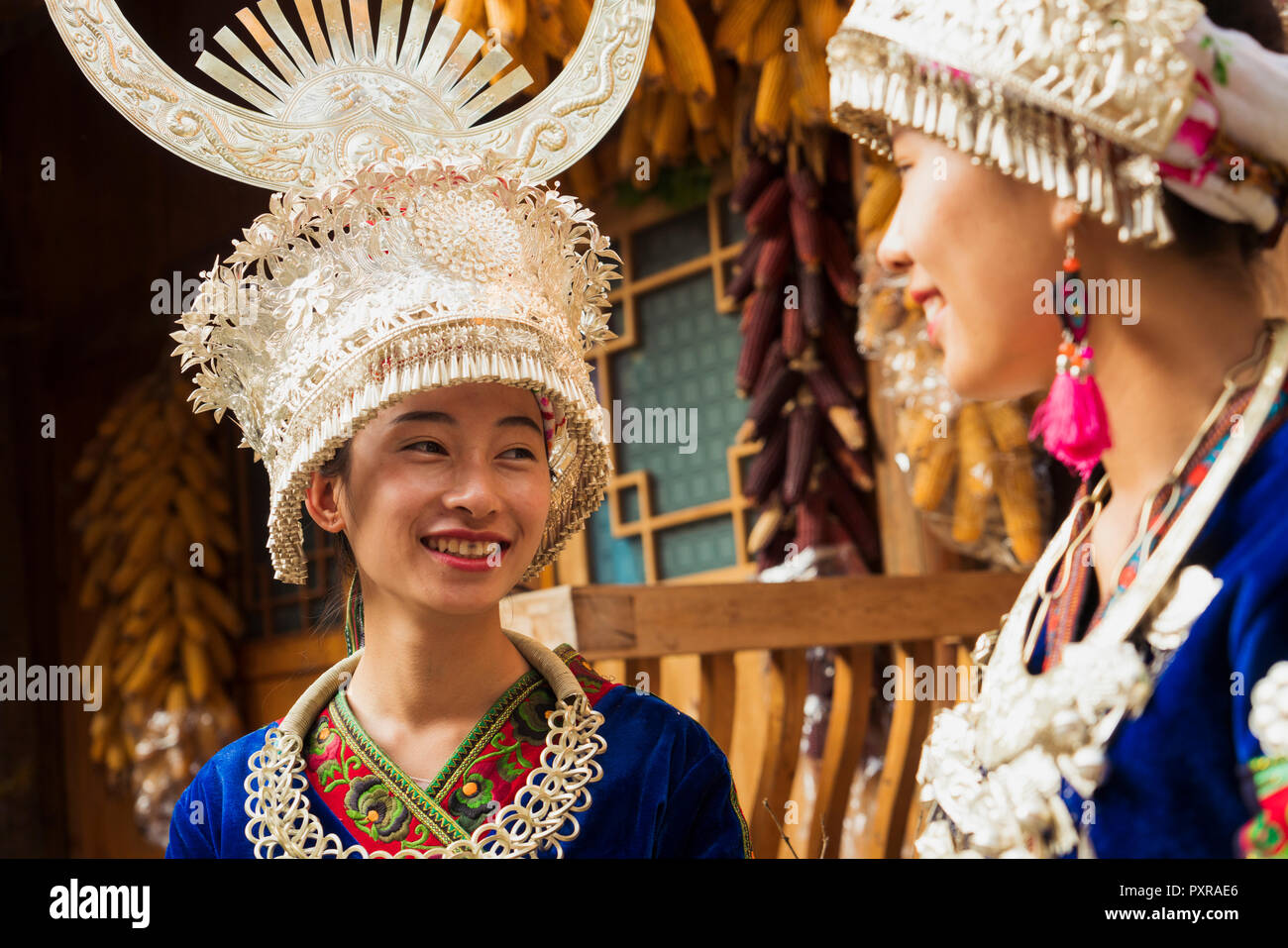 China, Yunnan, zwei lächelnde junge Miao Frauen in traditionellen Gewändern und Kopfbedeckungen Stockfoto