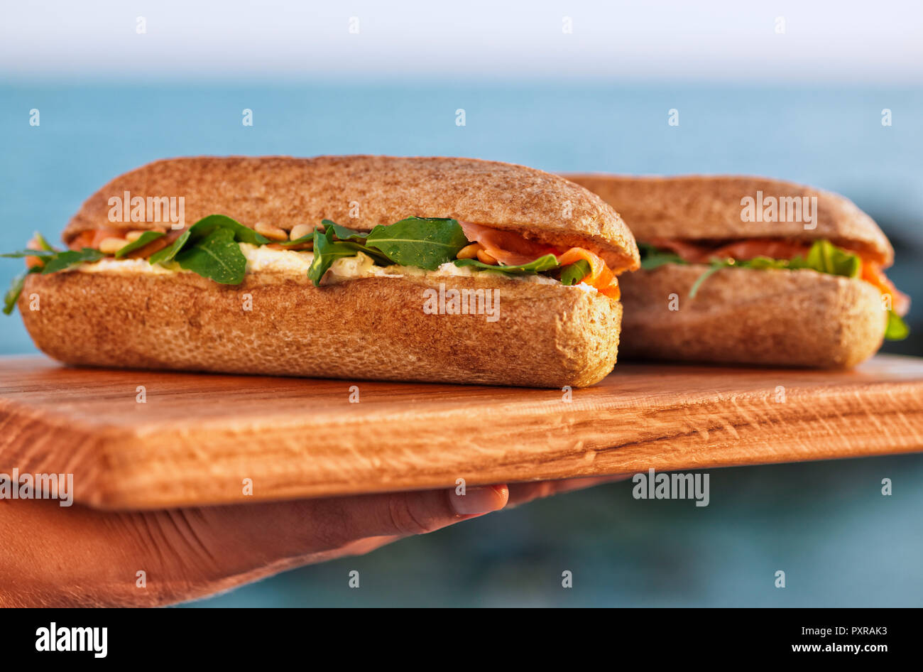 Woman's Hand Holzbrett mit zwei Lachs Sandwiches Stockfoto