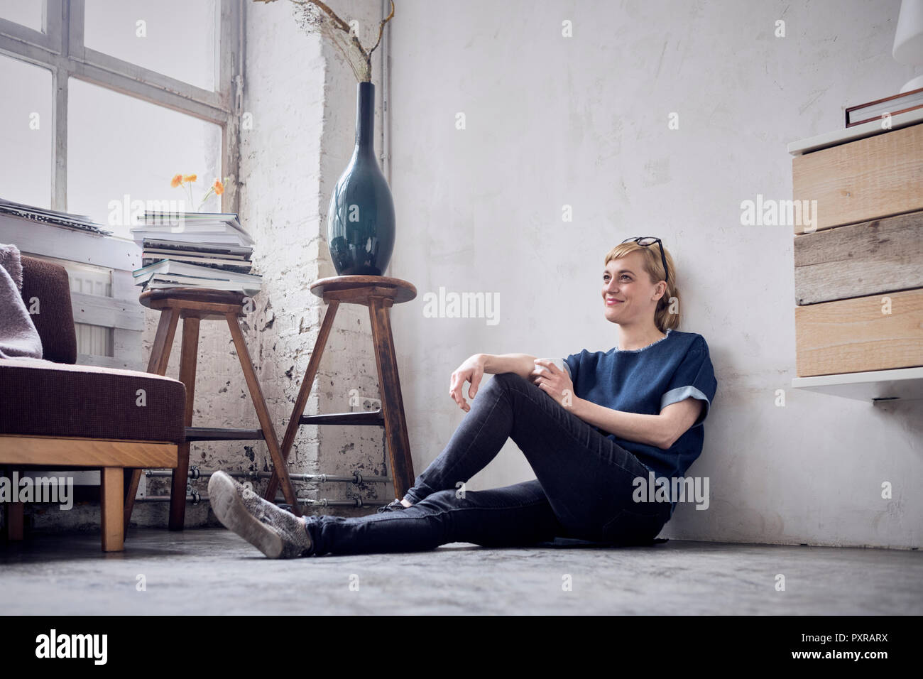 Lächelnde Frau auf dem Boden sitzend auf dem Dachboden Stockfoto