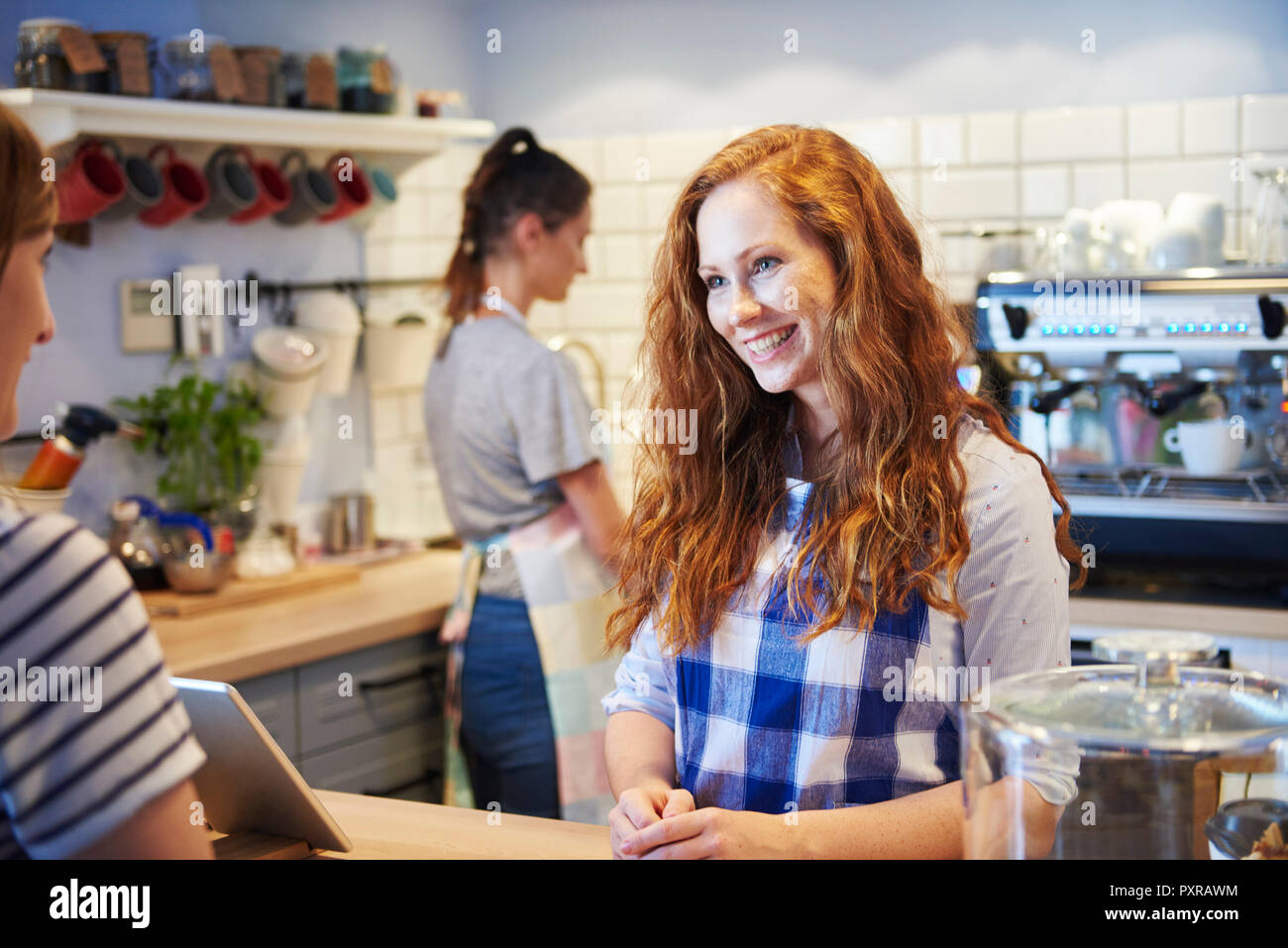 Lächelnde Kellnerin im Gespräch mit Kunden an der Theke in einem Cafe Stockfoto