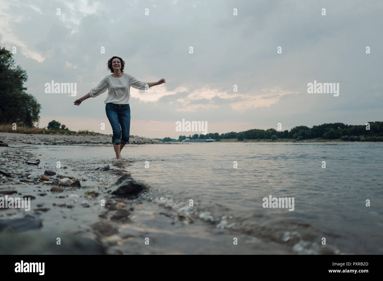 Lachende Frau am Flußufer läuft Stockfoto