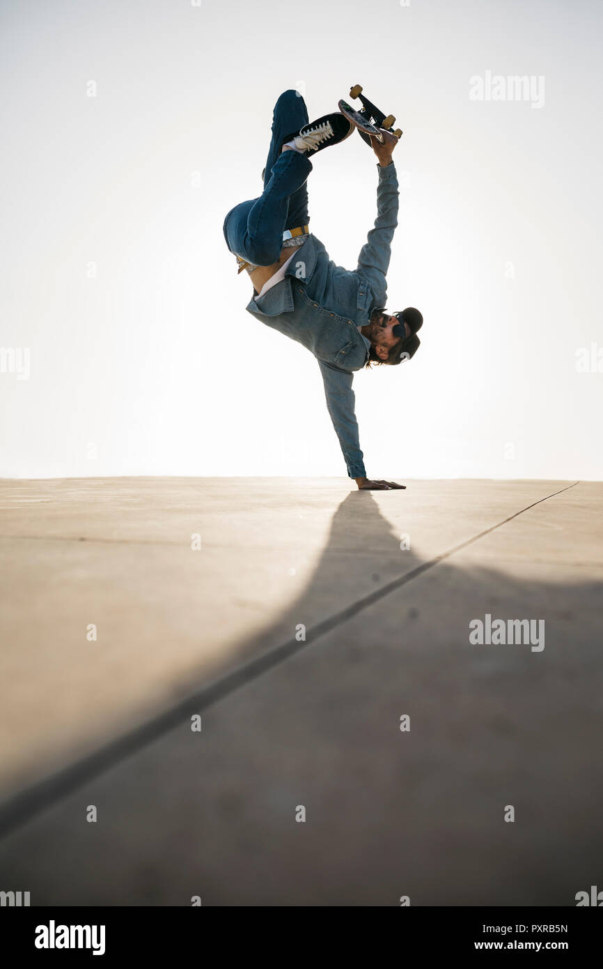 Stilvolle Mann in Jeans Outfit zeigen Trick mit Skate im Handstand Stockfoto