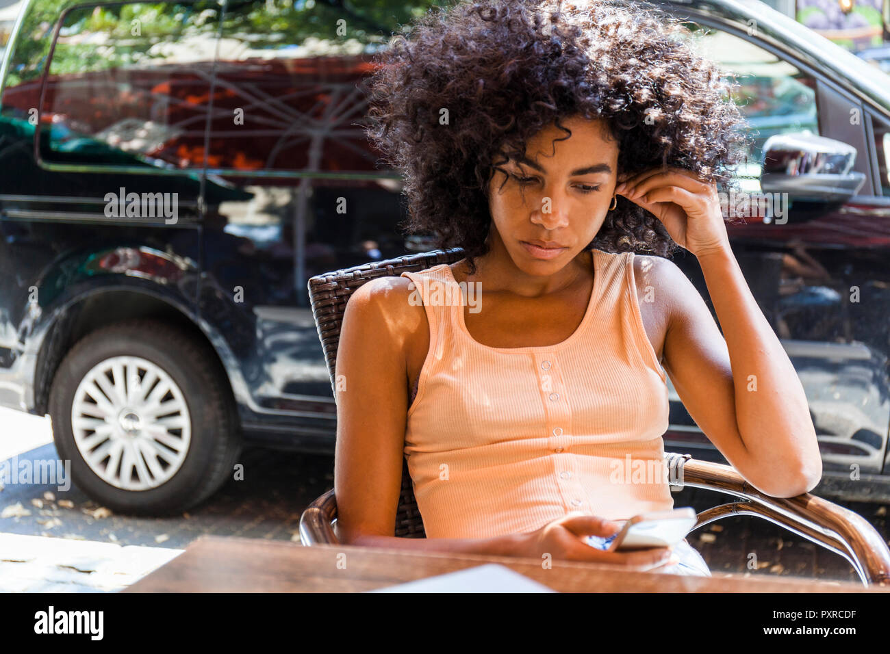 Porträt der jungen Frau mit dem lockigen Haar im Straßencafé in der Zelle Telefon sitzen Stockfoto