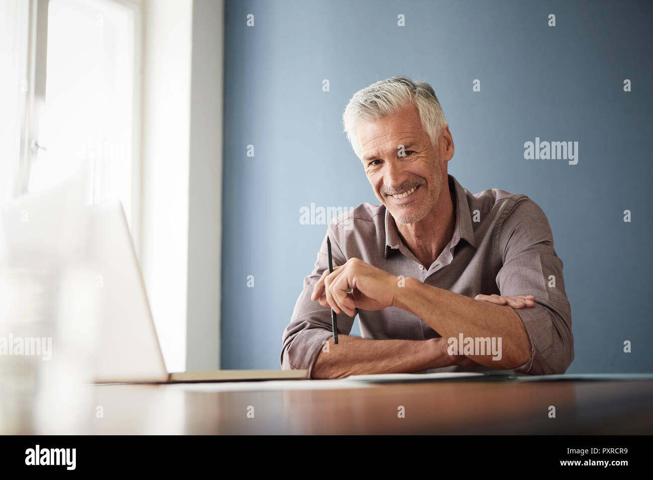 Portrait von zuversichtlich reifer Mann mit Laptop und Unterlagen zu Hause Stockfoto