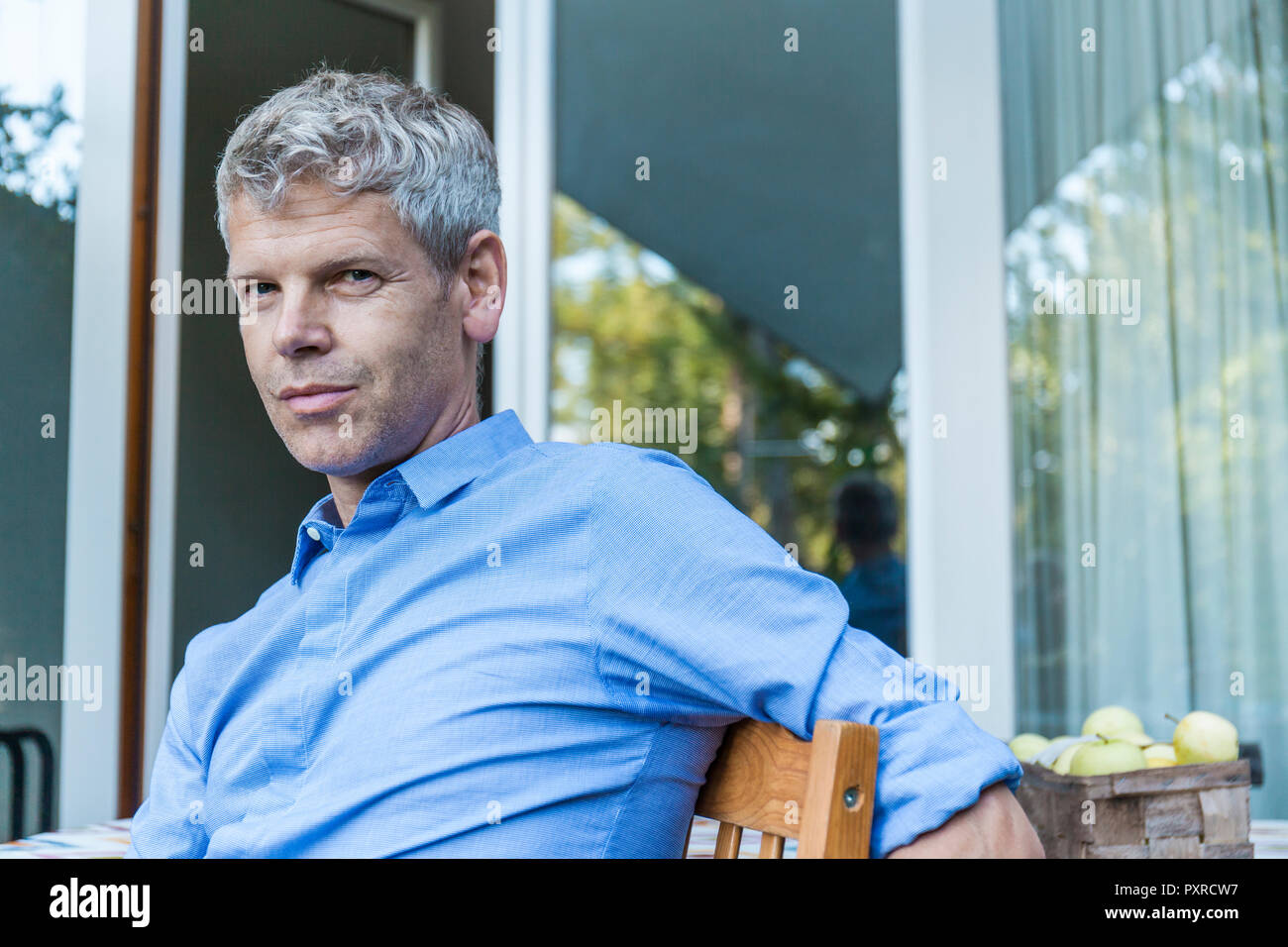 Portrait von reifer Mann mit dem grauen Haar sitzen auf der Terrasse tragen blaue T-Shirt Stockfoto