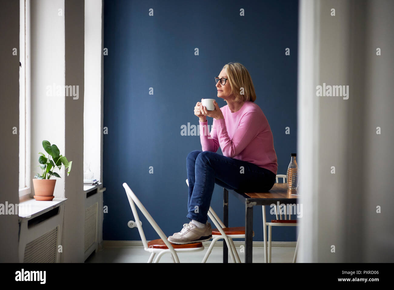 Reife Frau zu Hause mit Tasse Kaffee Blick aus Fenster Stockfoto