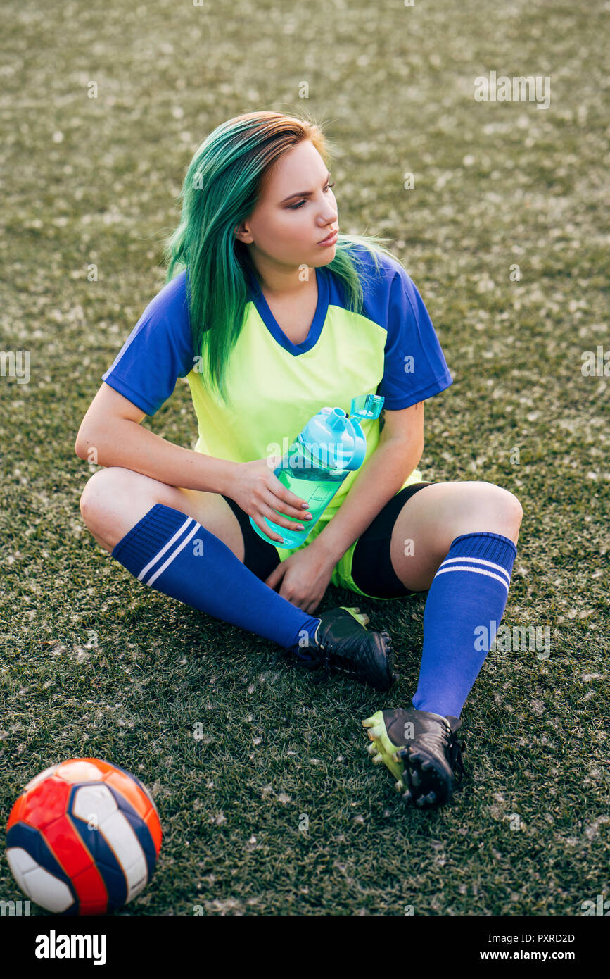 Junge Frau sitzt auf den Fußballplatz mit Wasserflasche und Kugel Stockfoto