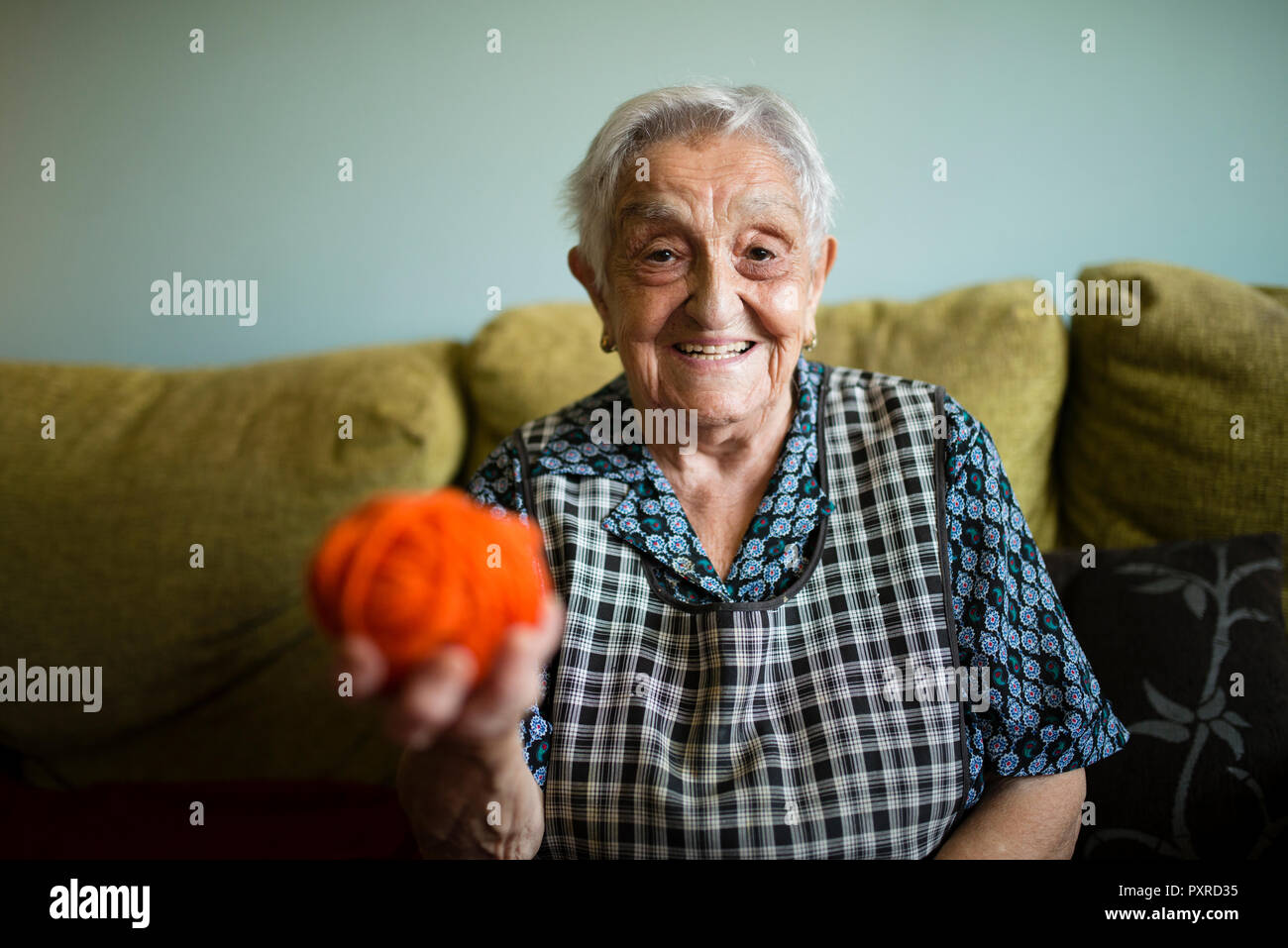 Portrait von lächelnden älteren Frau mit Wollknäuel sitzen auf der Couch zu Hause Stockfoto