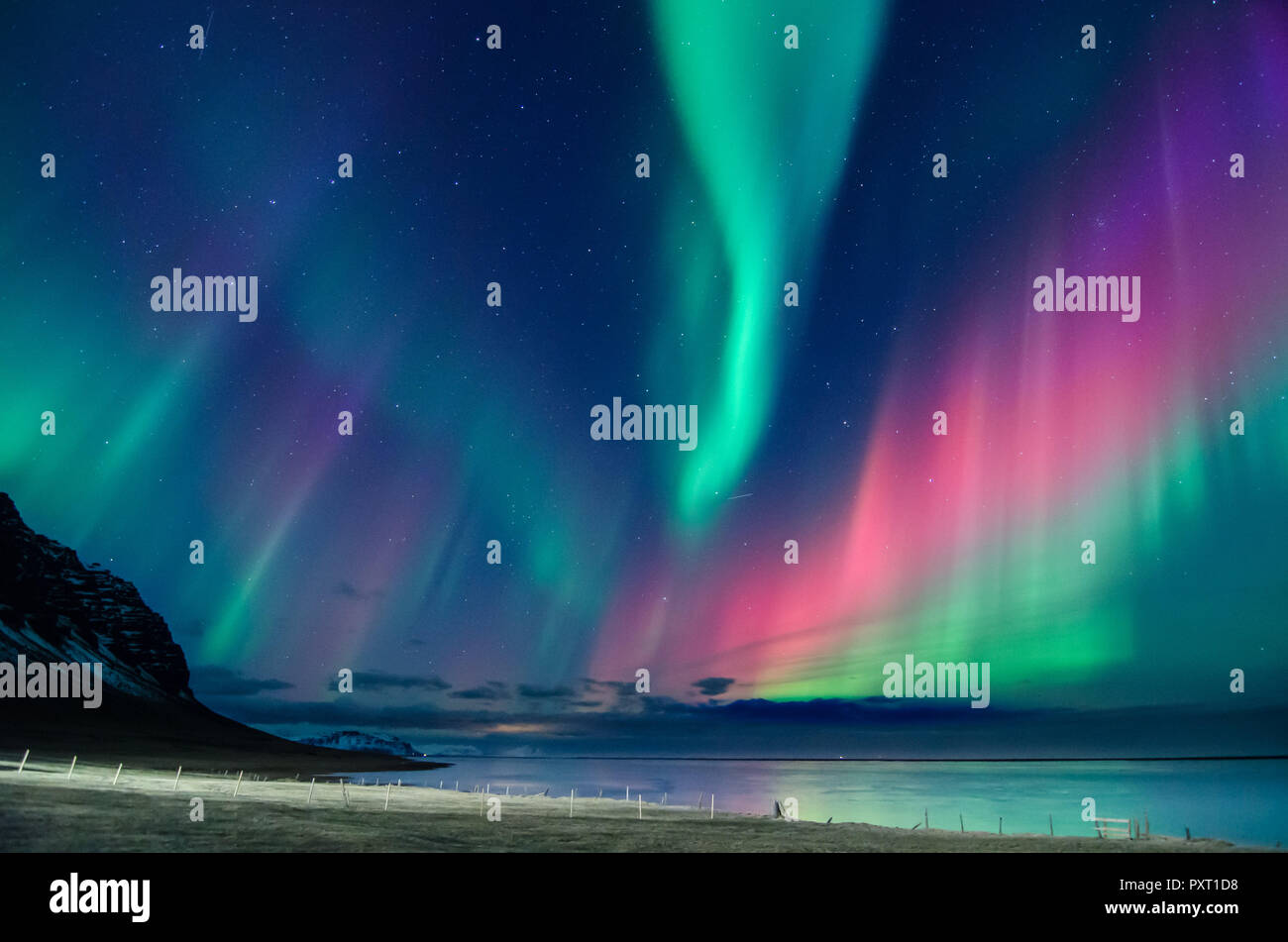 Bunte Nordlichter Aurora Borealis mit Grün, Blau, Lila rote Flammen über einen Strand im Süden von Island mit einem Berg auf der Rückseite Stockfoto