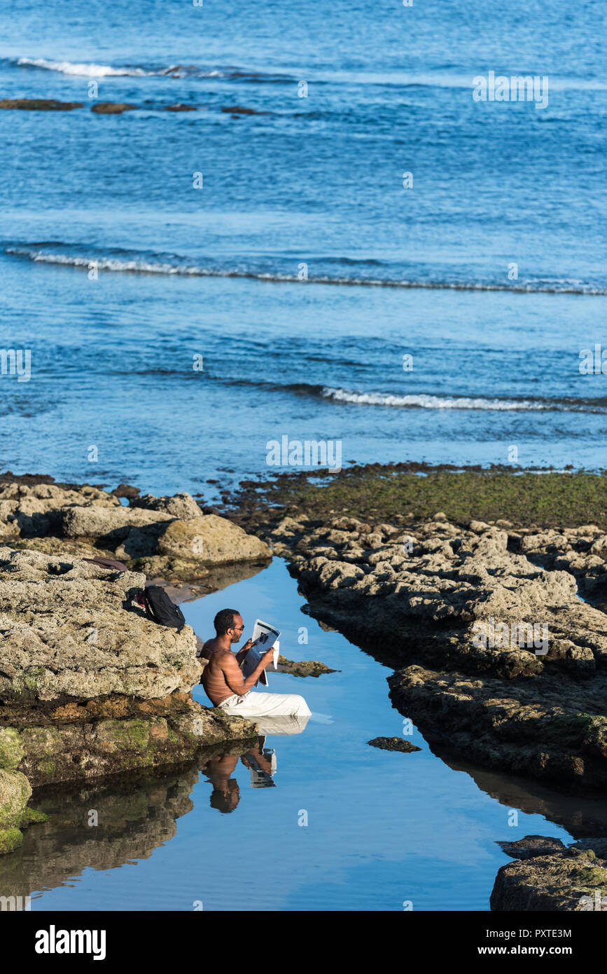 Estoril, Portugal - Juli 9, 2018: der Mann, der in Leinen Hose sitzen in Wassergefüllten rock Pool, der von den atlantischen Meer Lesen einer Zeitung am Nachmittag sonnen Stockfoto