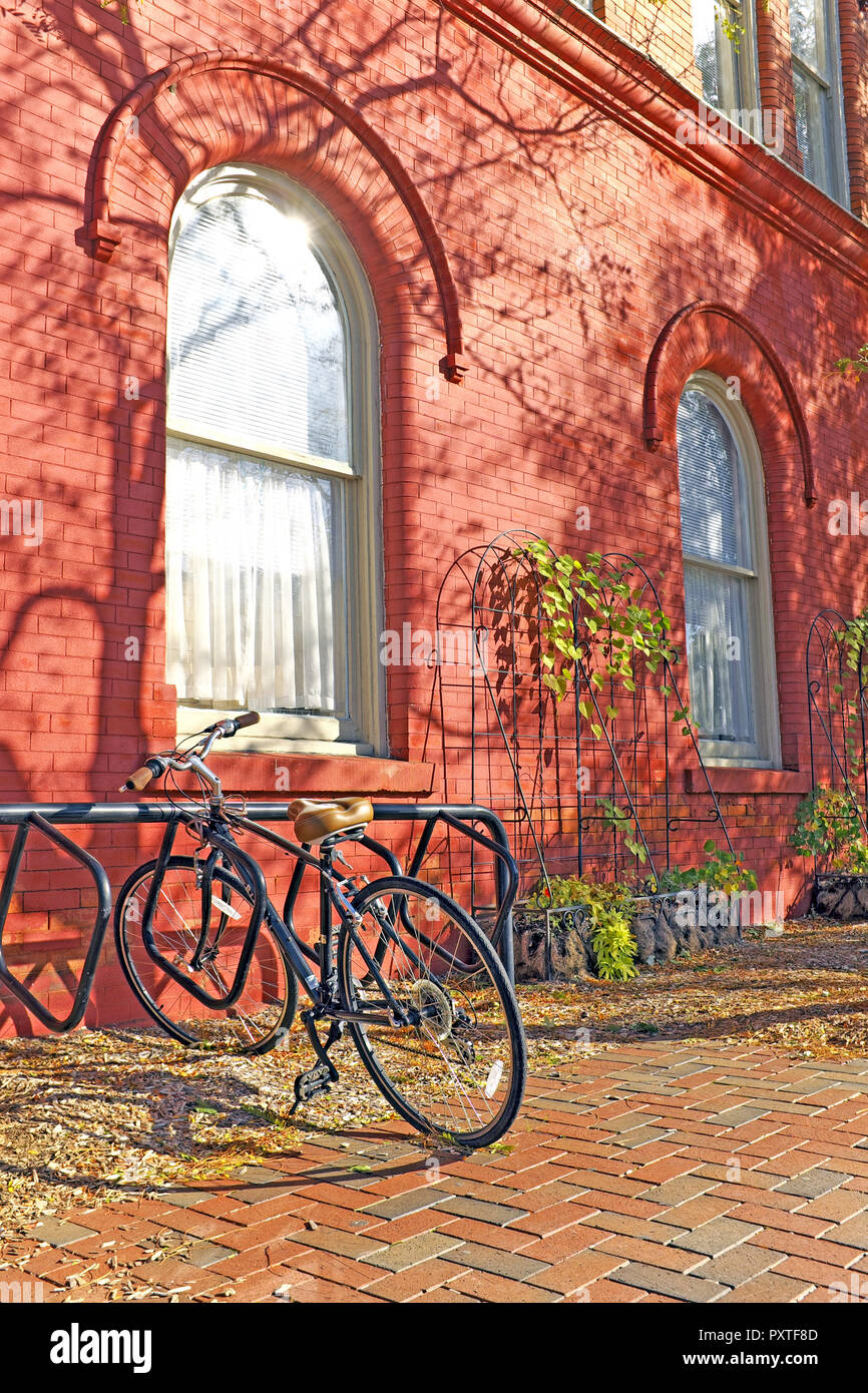 Ein Fahrrad ruht in einem Bike stehen auf der Seite der eine rote Birne farbige Gebäude in der Innenstadt von Willoughby, Ohio, USA auf einen Tag fallen. Stockfoto