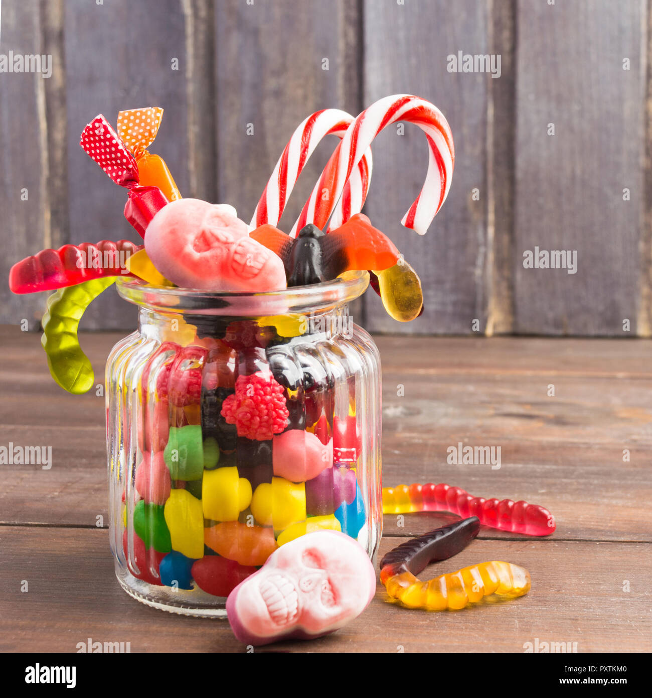 Glas Glas mit Süßigkeiten für Halloween auf hölzernen Hintergrund, Quadrat Schuß Stockfotografie