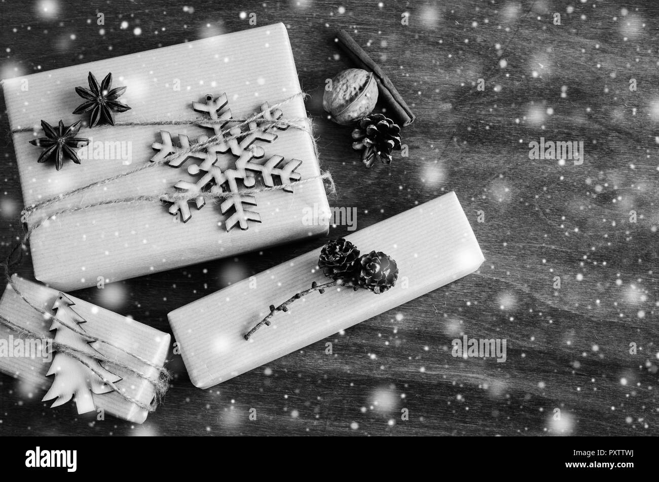 Kraftpapier Kartons mit Geschenken dekoriert mit Holzmöbeln Schneeflocke, Weihnachtsbaum und Jute auf Holz- Hintergrund. Vintage Bild mit gezogenen Schneefall. Weihnachten in Stockfoto