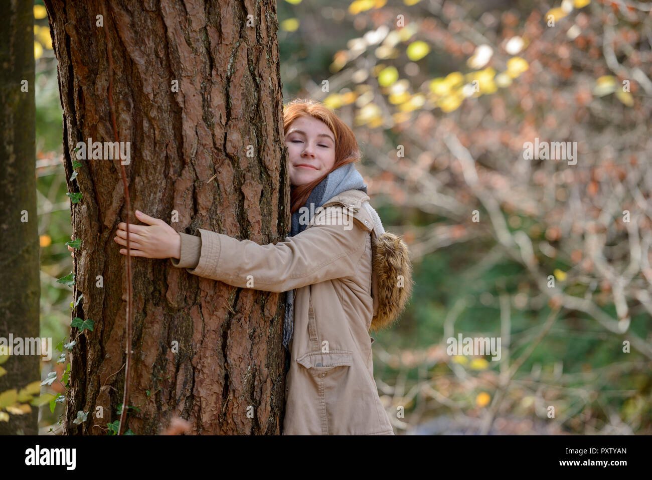Portrait Of Smiling teenage Mädchen umarmt Baum im herbstlichen Wald Stockfoto