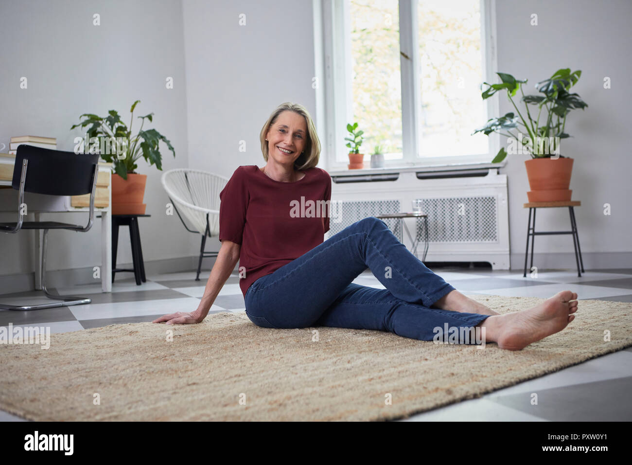 Lächelnd reife Frau auf dem Boden zu Hause sitzen Stockfoto