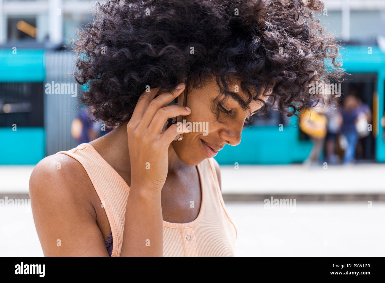 Deutschland, Frankfurt, Portrait von lächelnden jungen Frau mit lockigem Haar auf dem Telefon Stockfoto