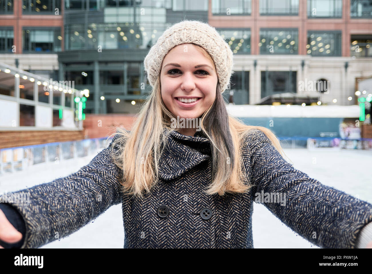 Blonde junge Frau mit Blick auf die Kamera beim Skifahren auf einer Eisbahn Stockfoto