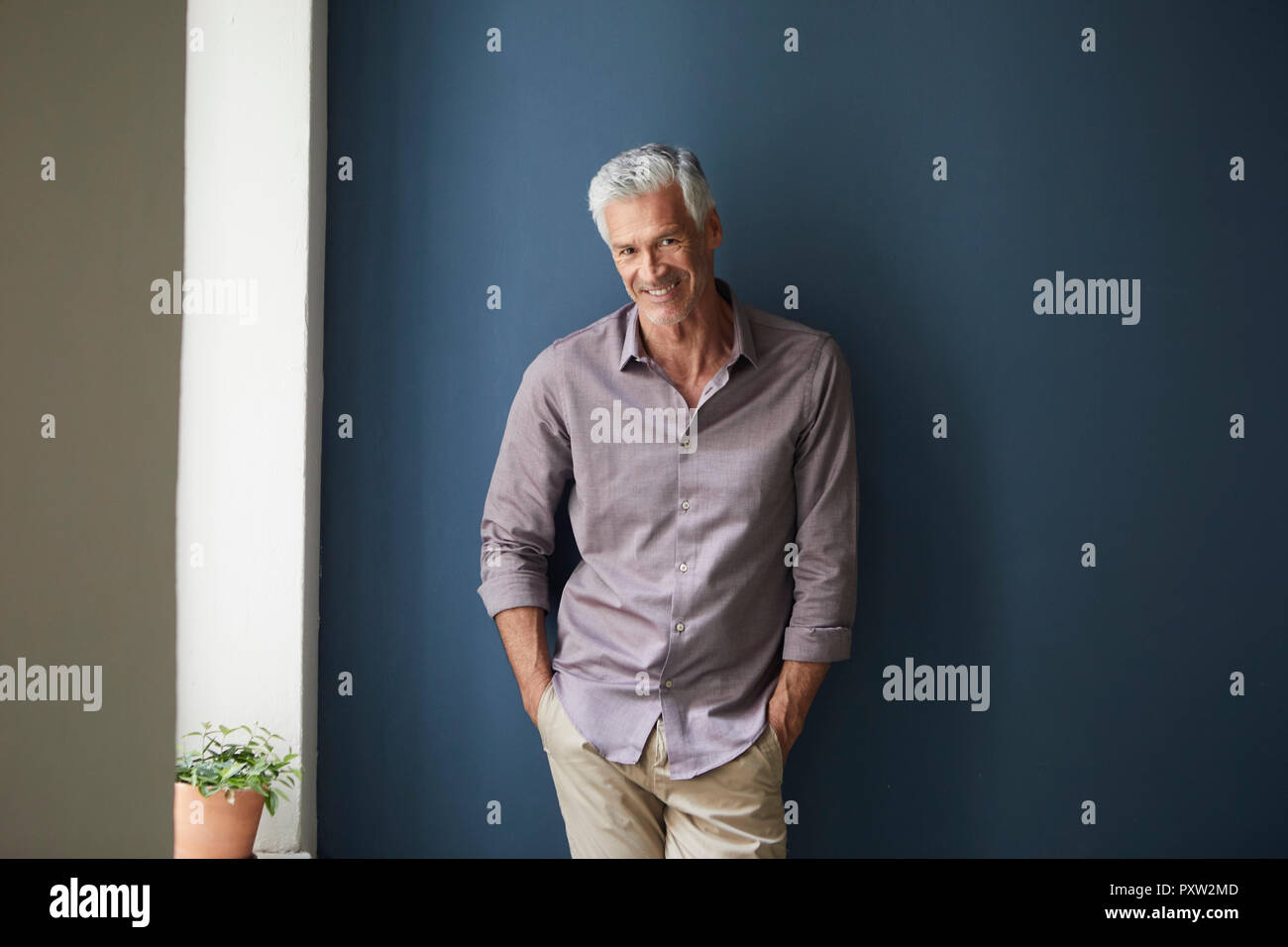 Portrait von zuversichtlich reifer Mann zu Hause gegen blaue Wand lehnt Stockfoto