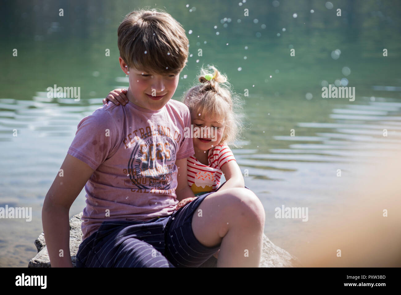 Bruder und Schwester sitzen auf Boulder an einem See mit geschlossenen Augen Stockfoto