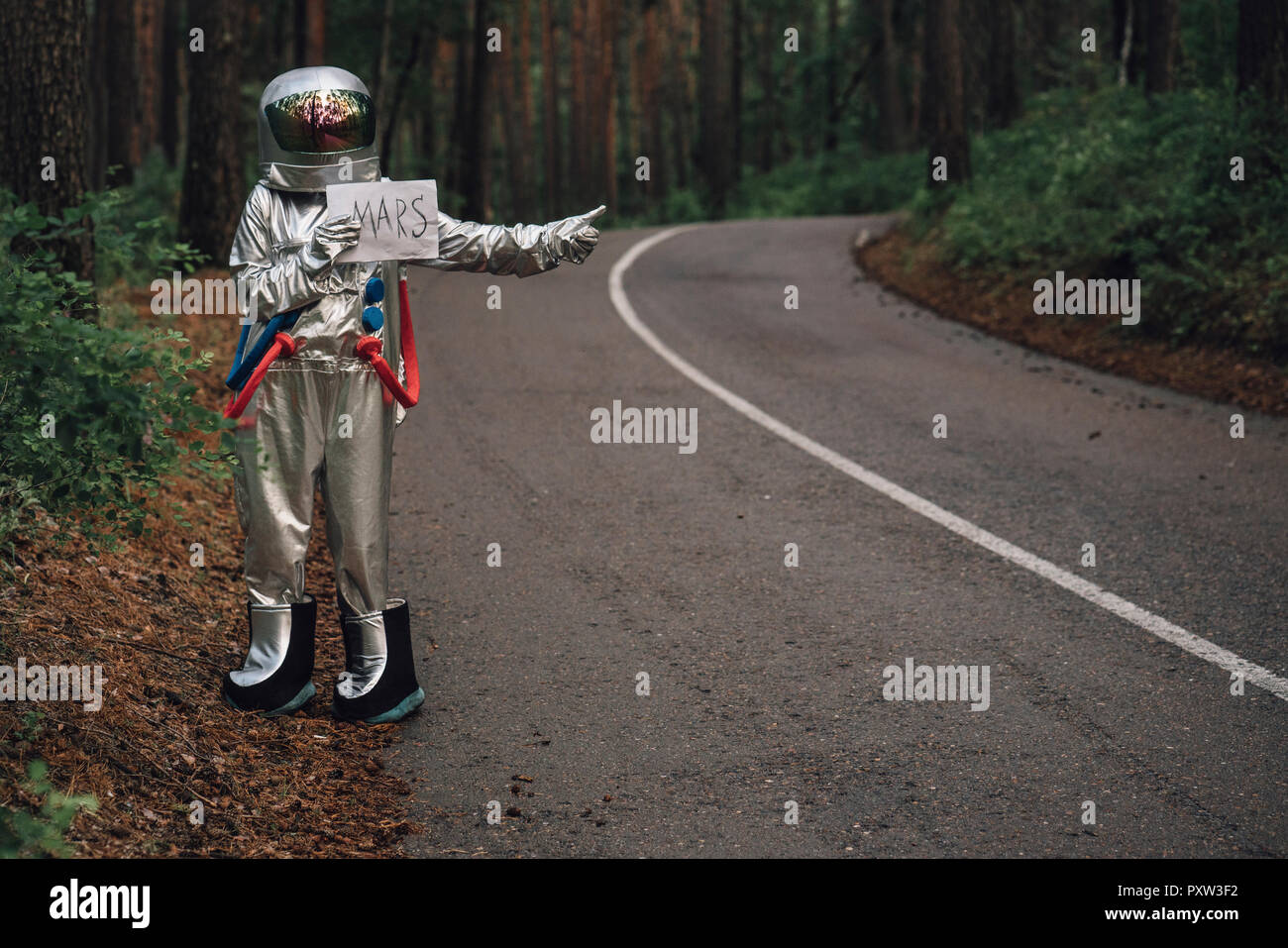 Spaceman per Anhalter zum Mars, stehend auf der Straße im Wald Stockfoto