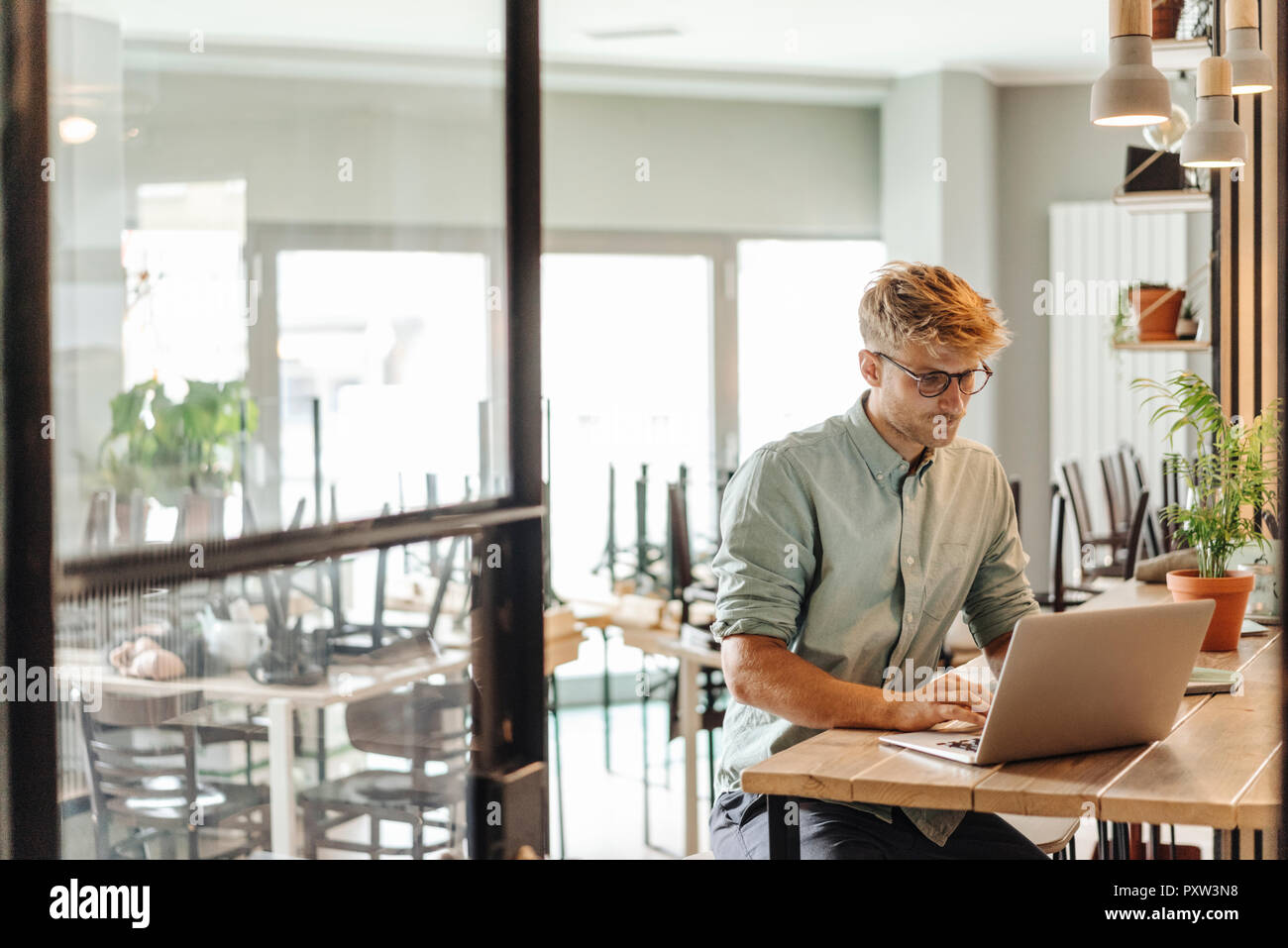 Junger Mann bei der Arbeit in seinem Start-up-Cafe, mit Laptop Stockfoto
