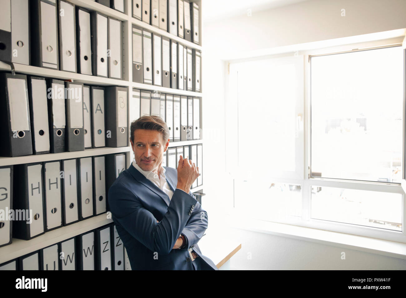 Unternehmer im Unternehmen Archiv, lehnte sich gegen Regal mit Dateien Stockfoto