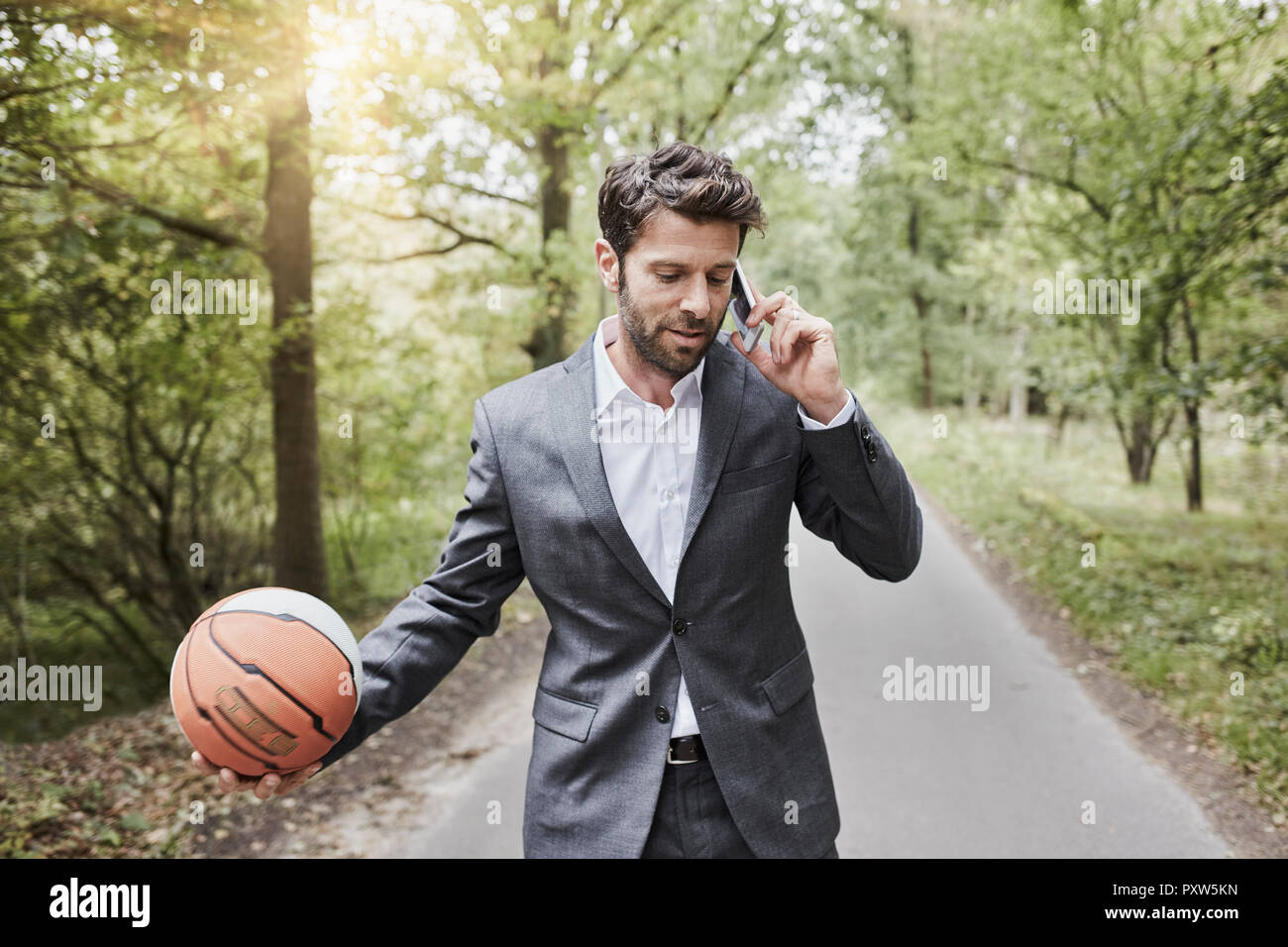 Geschäftsmann mit Basketball sprechen auf dem Smartphone auf die ländliche Straße Stockfoto